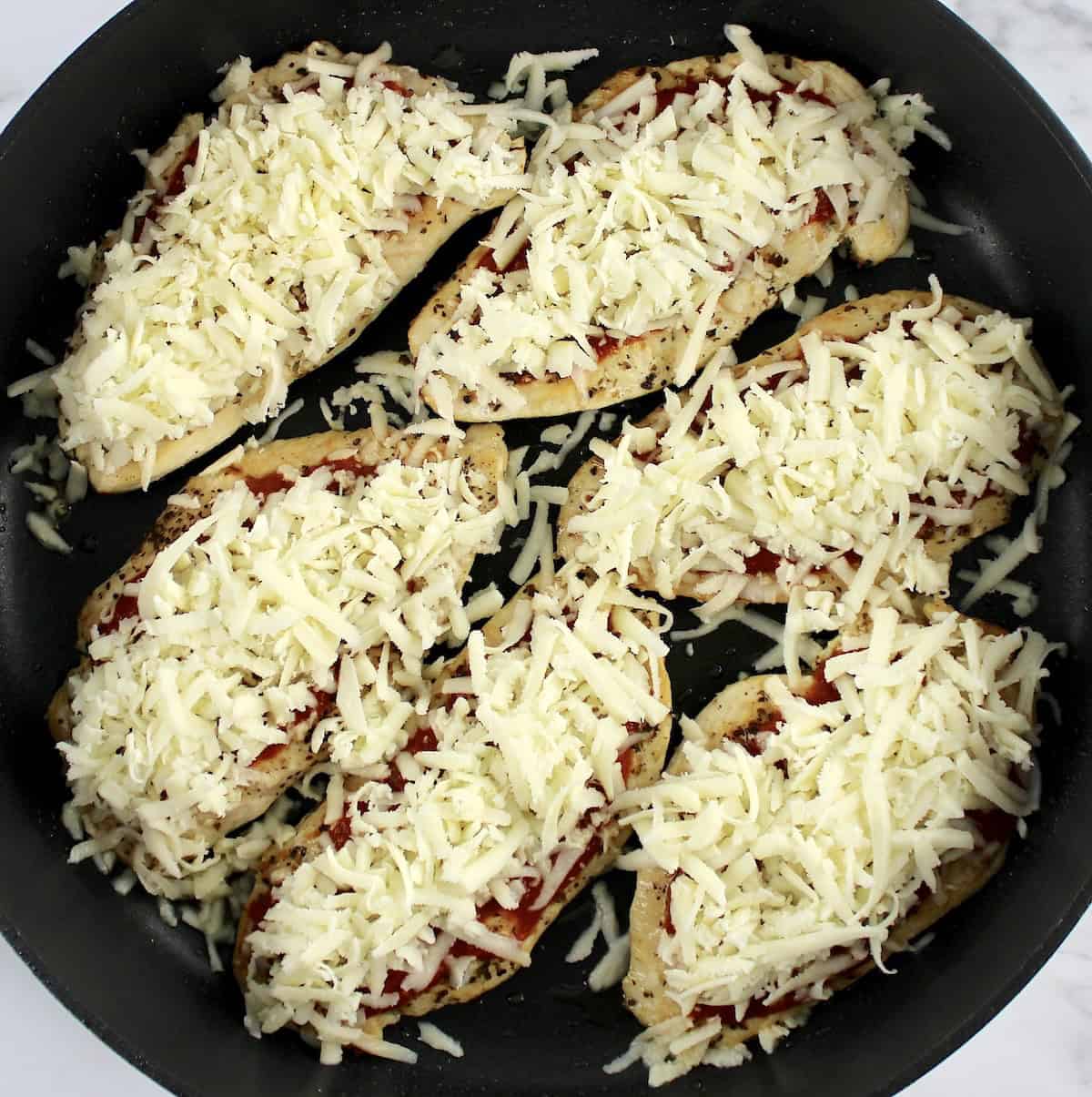 6 pieces of chicken with shredded mozzarella on top in skillet