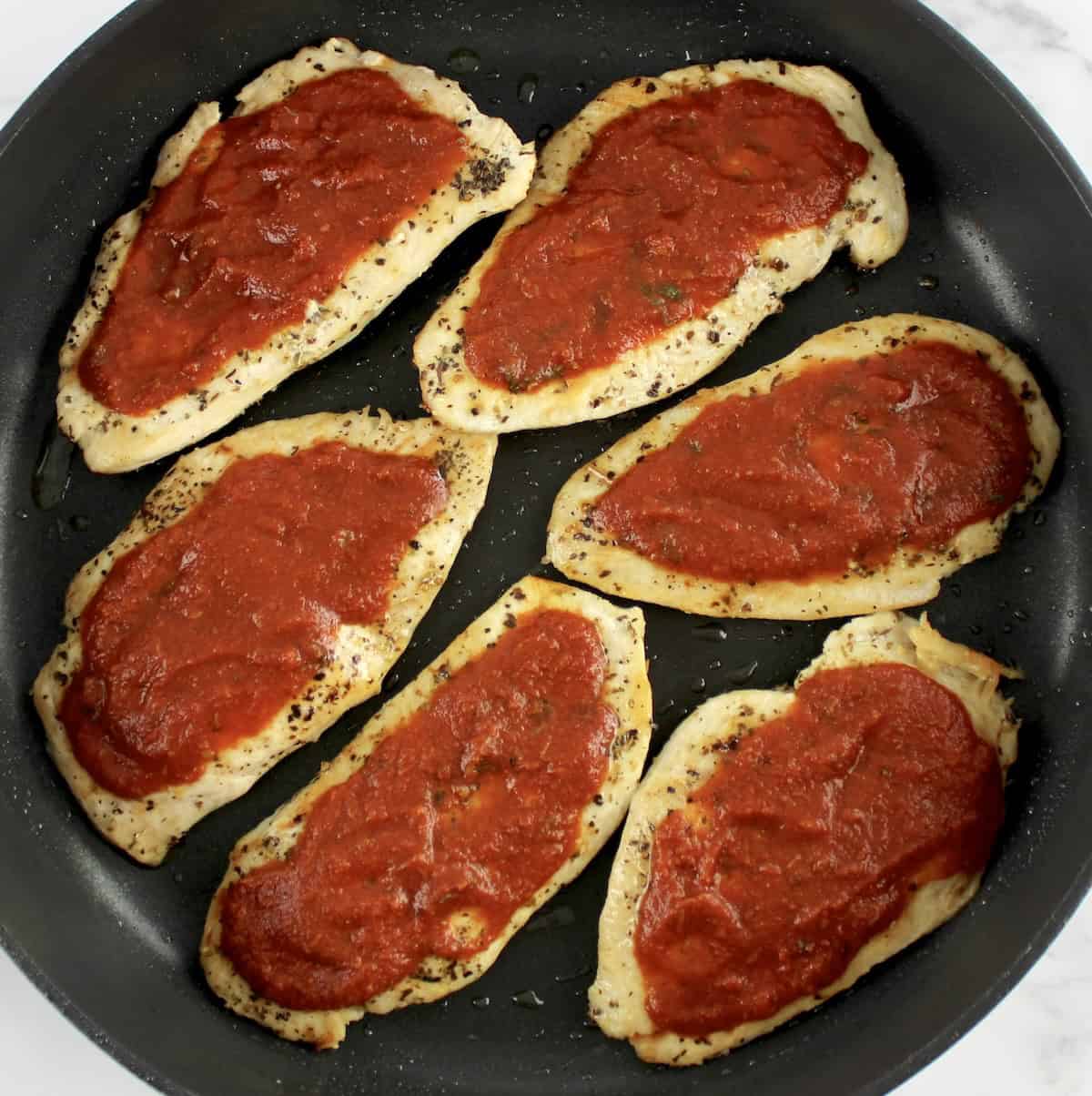 6 pieces of cooked chicken in skillet with pizza sauce on tops