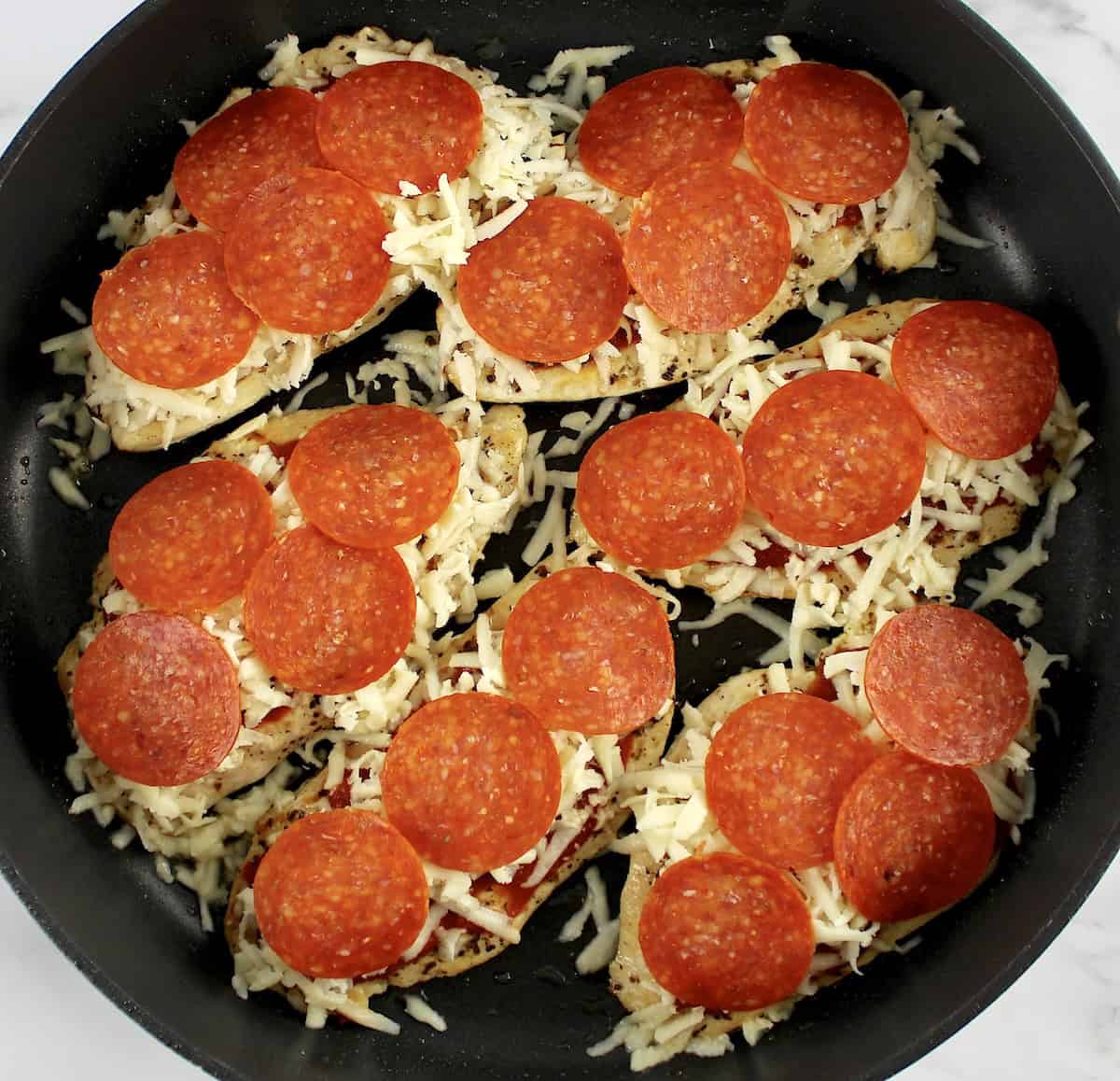 6 pieces of chicken in skillet with shredded mozzarella and slices of pepperoni on top