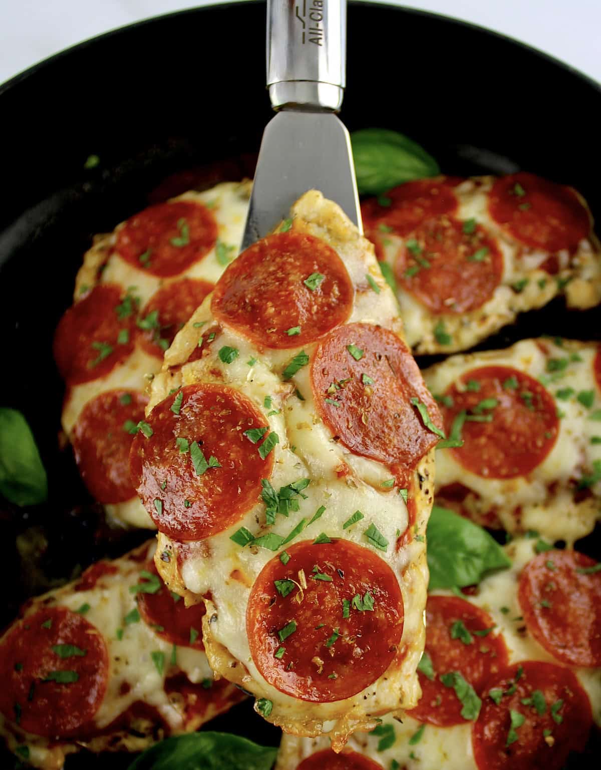 Pizza Chicken being held up with silver spatula over skillet