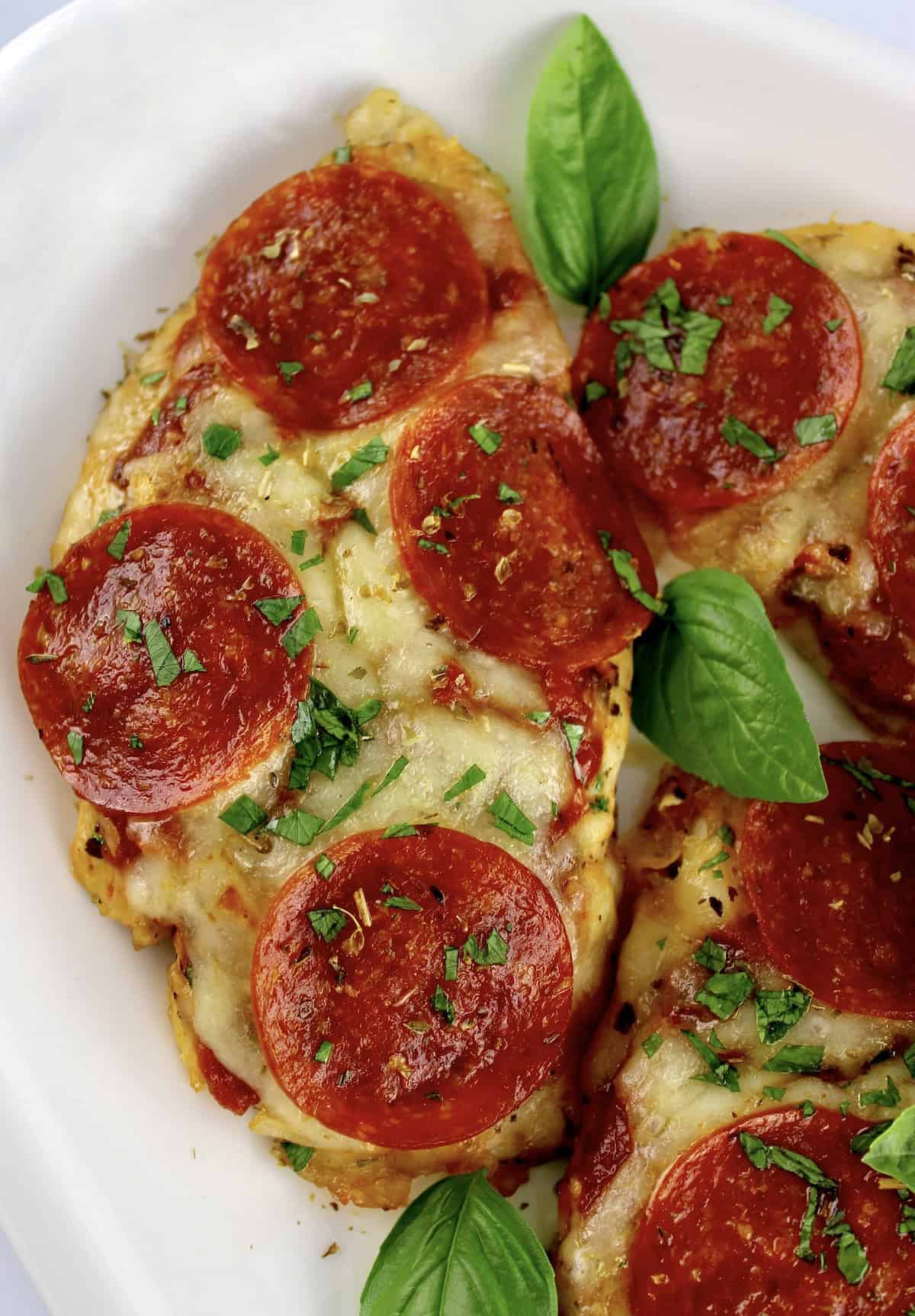 closeup of Pizza Chicken on white plate with fresh basil leaves