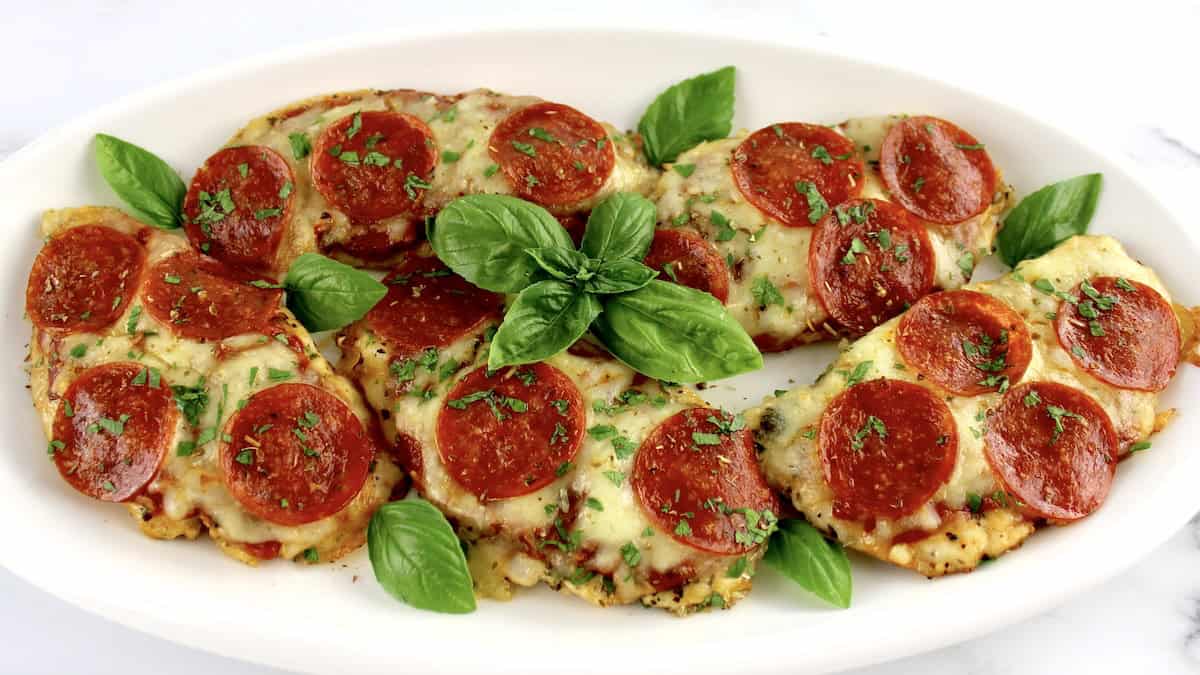 5 pieces of Pizza Chicken on white oval platter and fresh basil garnish