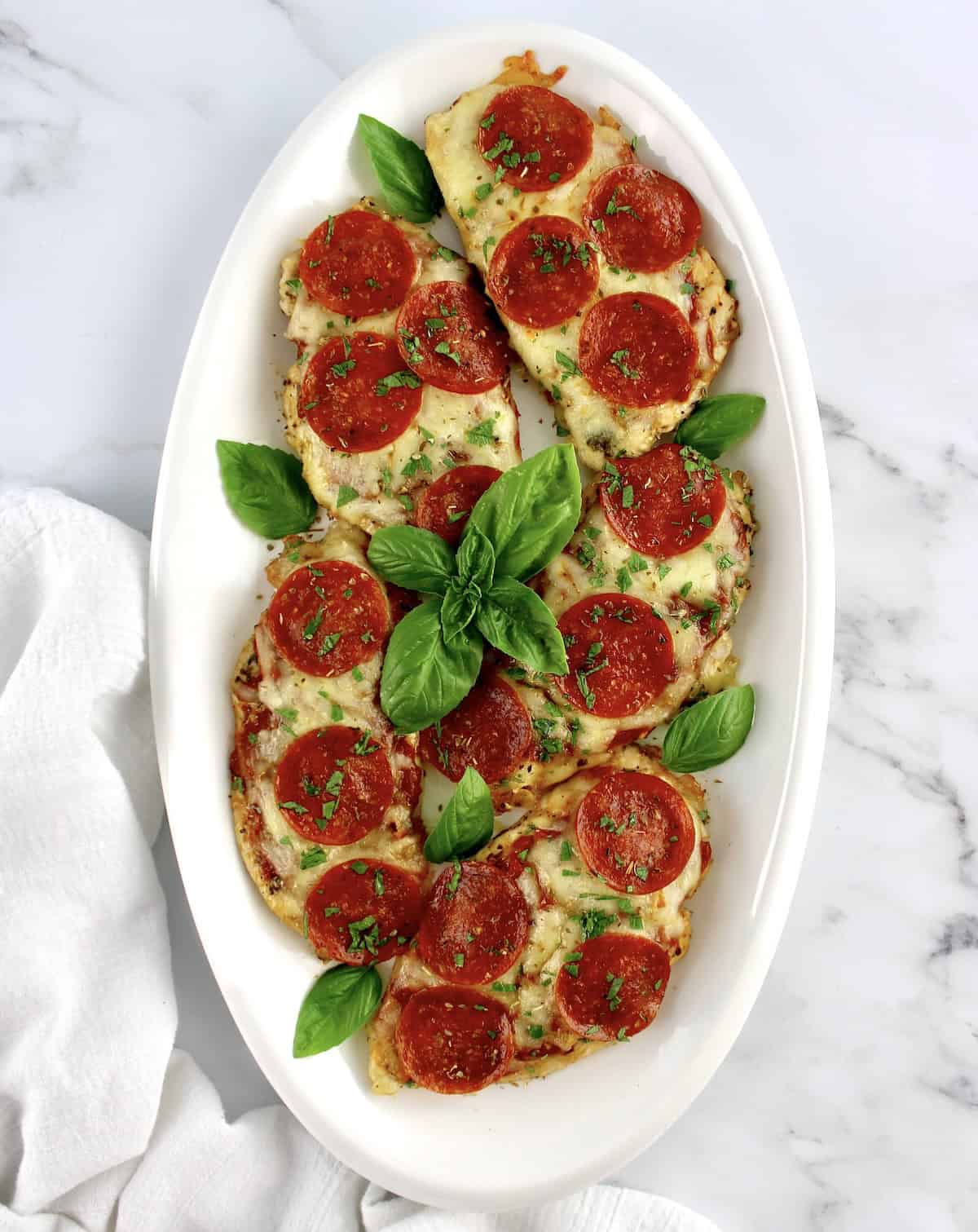 overhead view of 5 pieces of Pizza Chicken on white oval platter with fresh basil