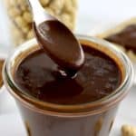 Sugar-Free Nutella being spooned out of glass jar with hazelnuts in glass jar in back