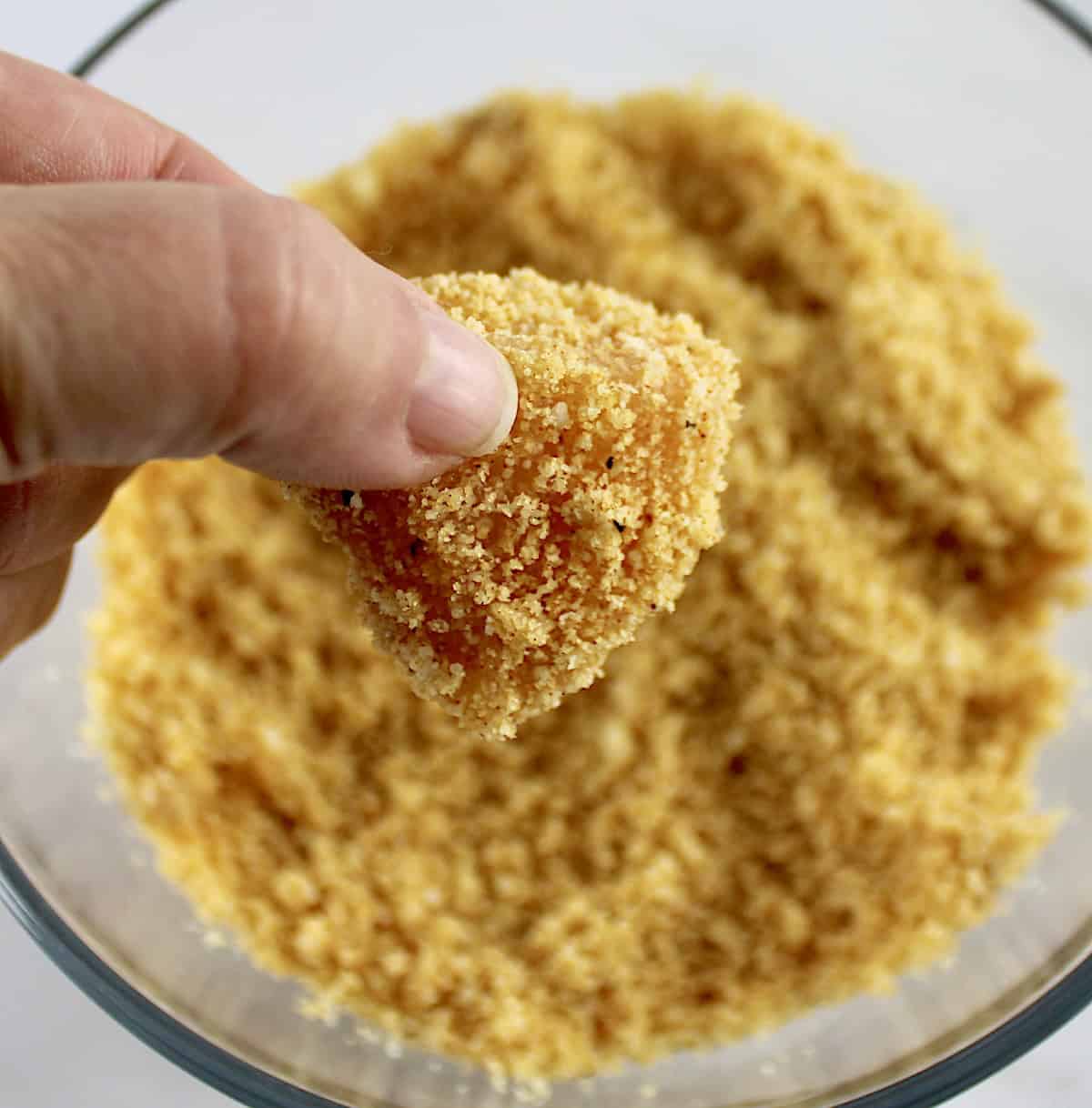 holding up Air Fryer Chicken Nugget uncooked over glass bowl with breading