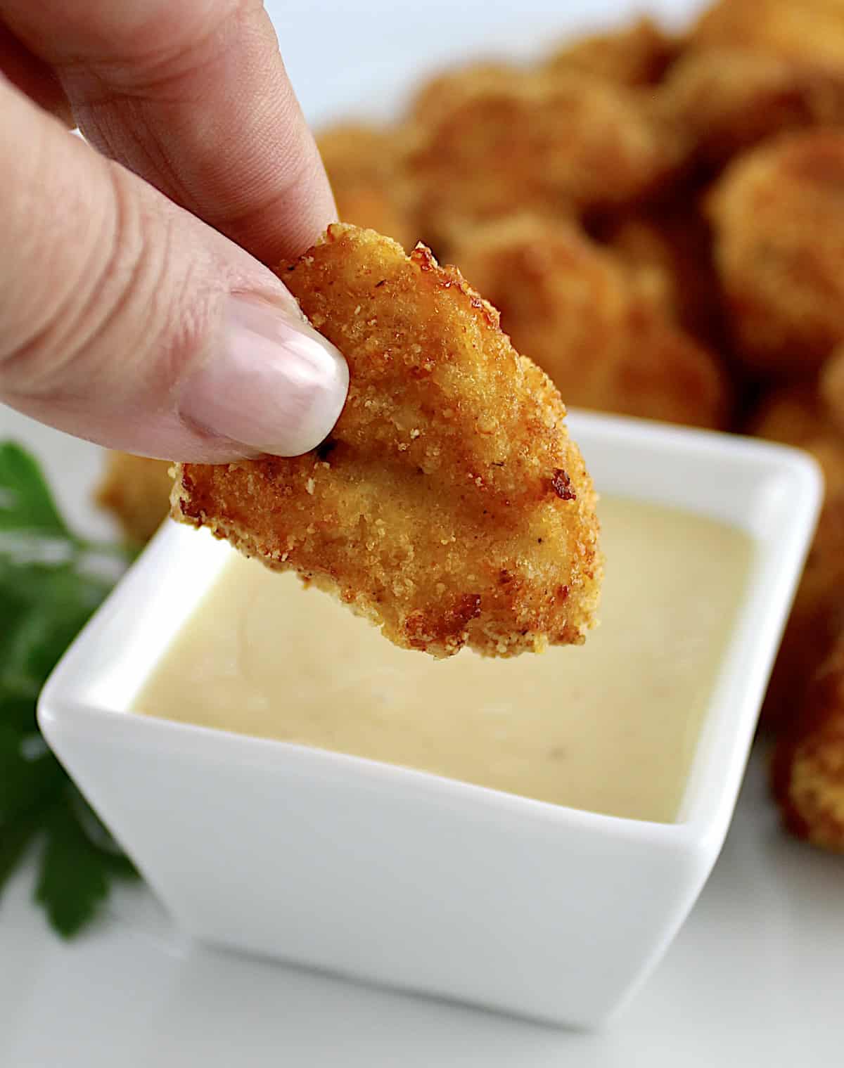 holding chicken nugget over honey mustard sauce in white bowl