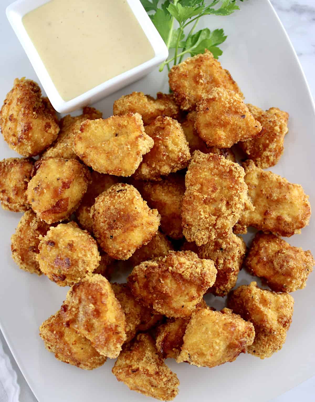 overhead view of Air Fryer Chicken Nuggets on white plate with honey mustard sauce and parsley sprig