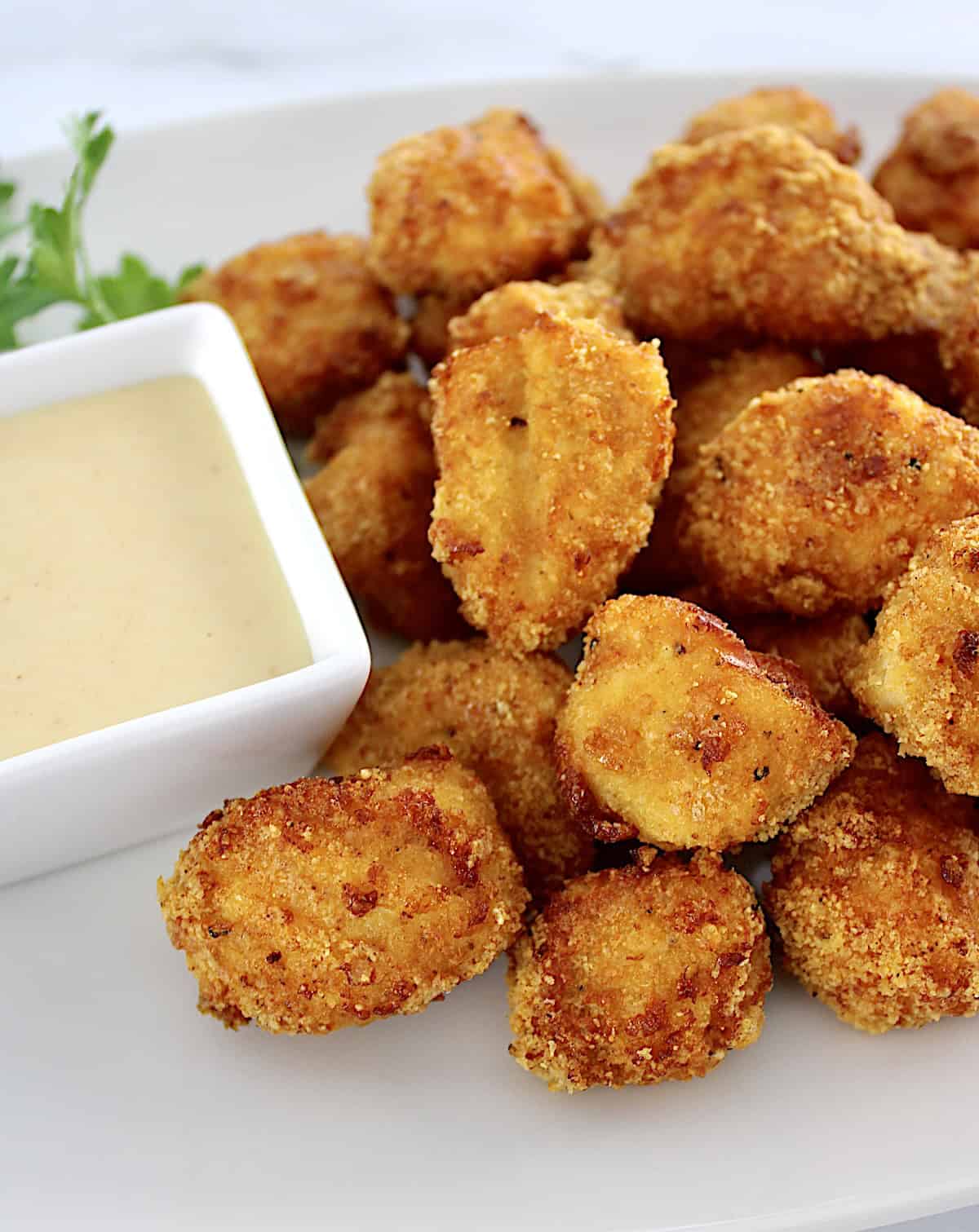 closeup of Air Fryer Chicken Nuggets on white plate with honey mustard sauce in white cup on side