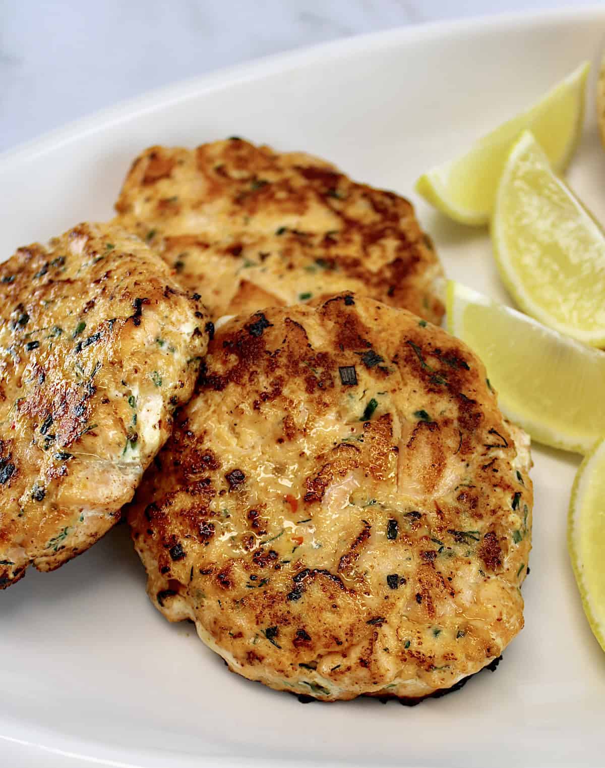 closeup of 3 salmon patties on white plate with lemon wedges