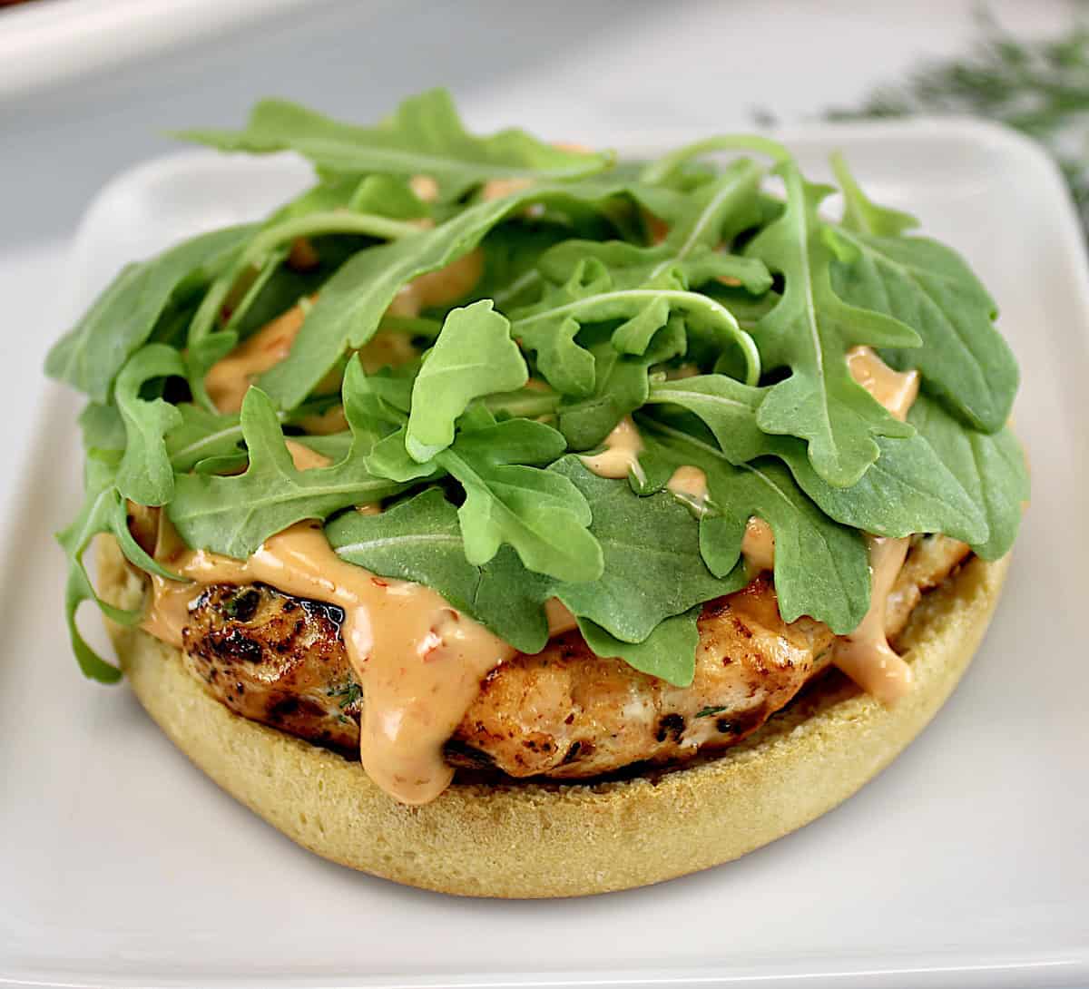 Boom Boom Salmon Burger on white plate with sauce and arugula on top