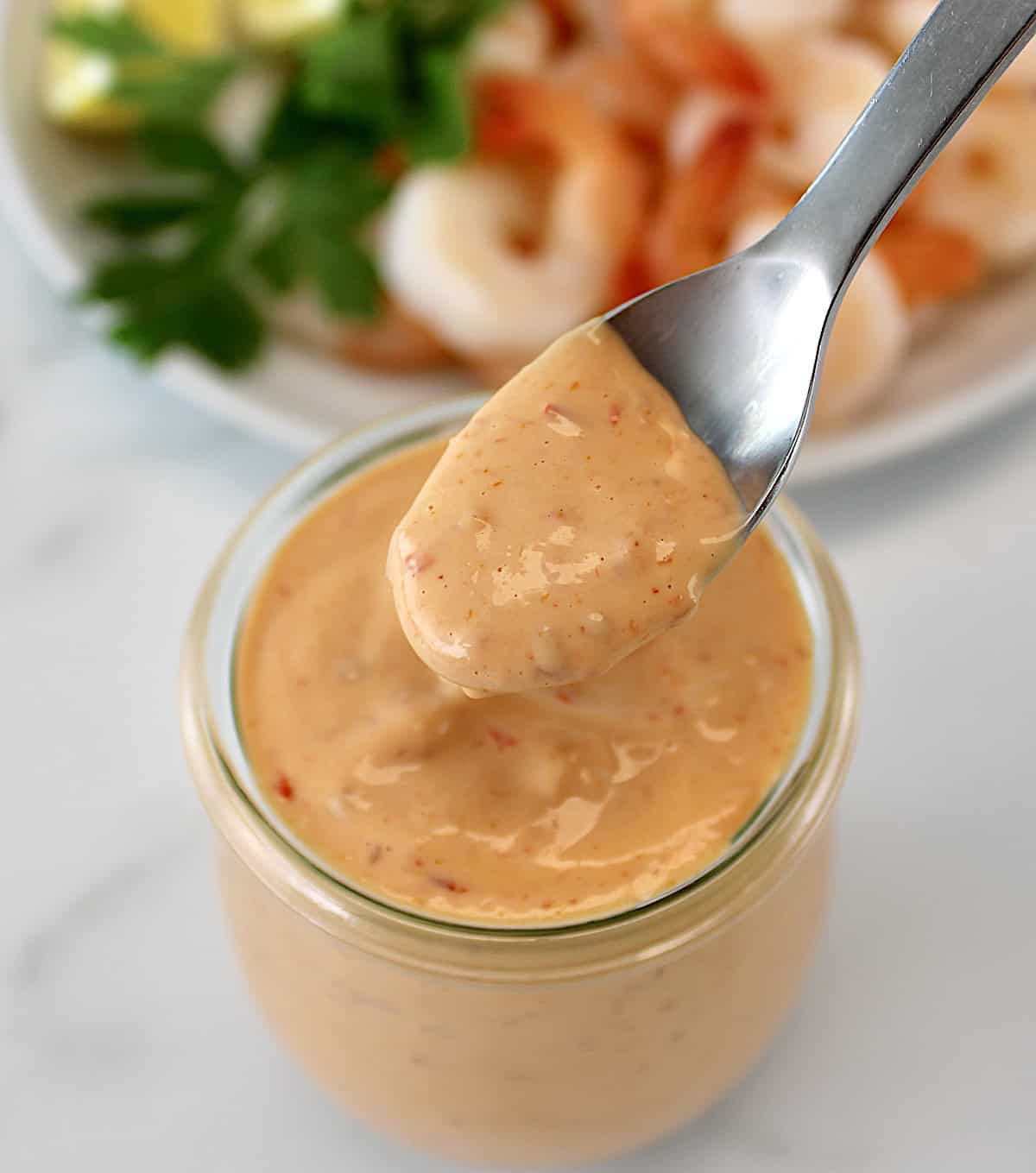 Boom Boom Sauce in glass jar being spooned out with shrimp in back