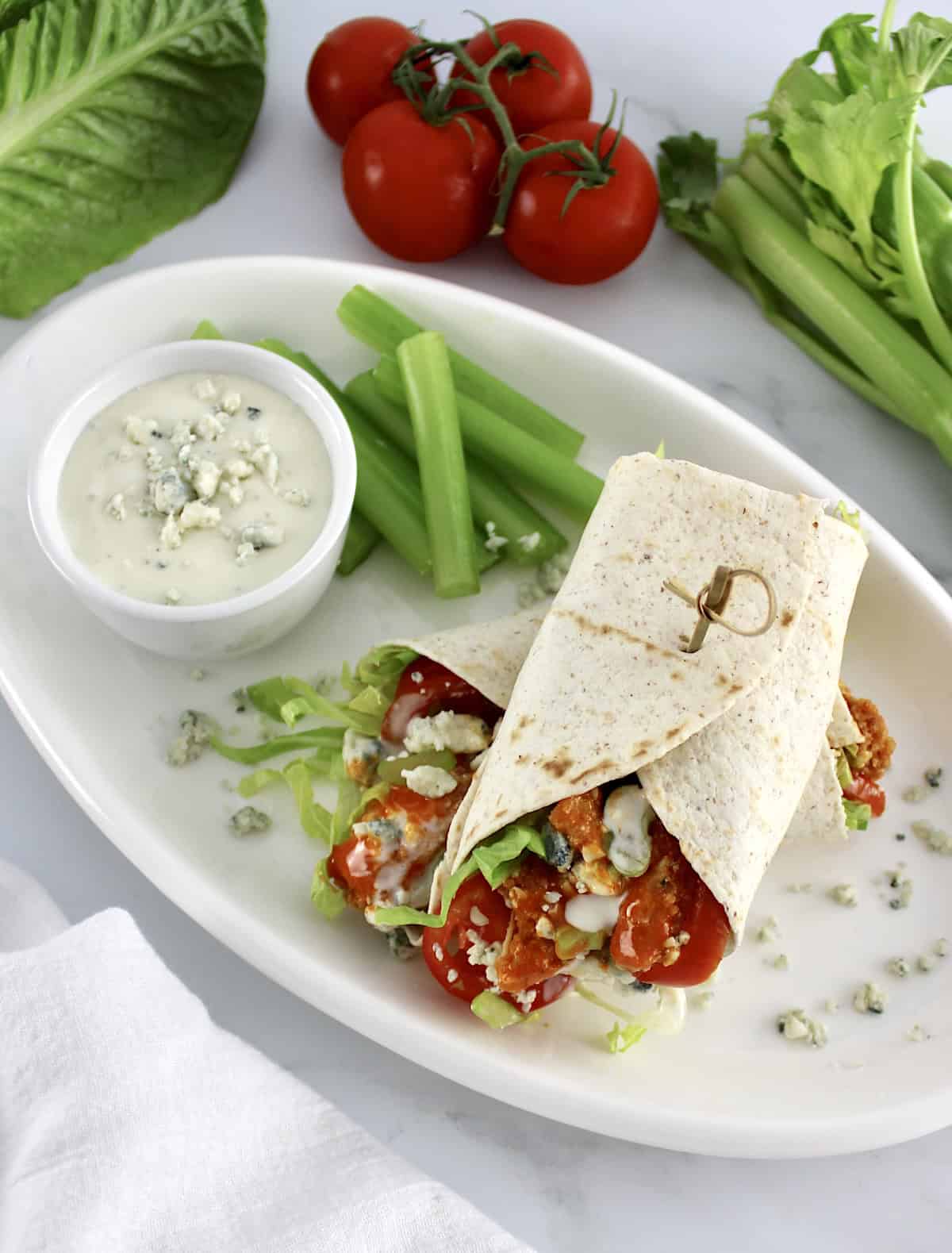 overhead view of Buffalo Chicken Wrap on white plate with celery and blue cheese on side