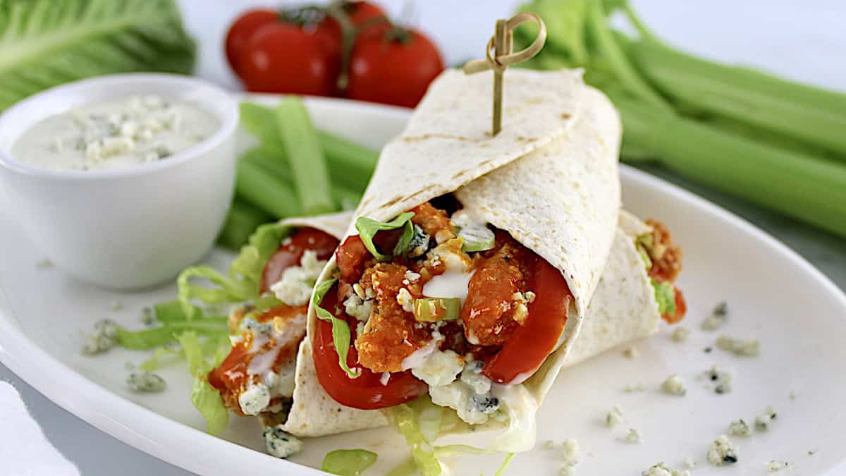 Buffalo Chicken Wrap cut in half on white plate with blue cheese and celery sticks on side