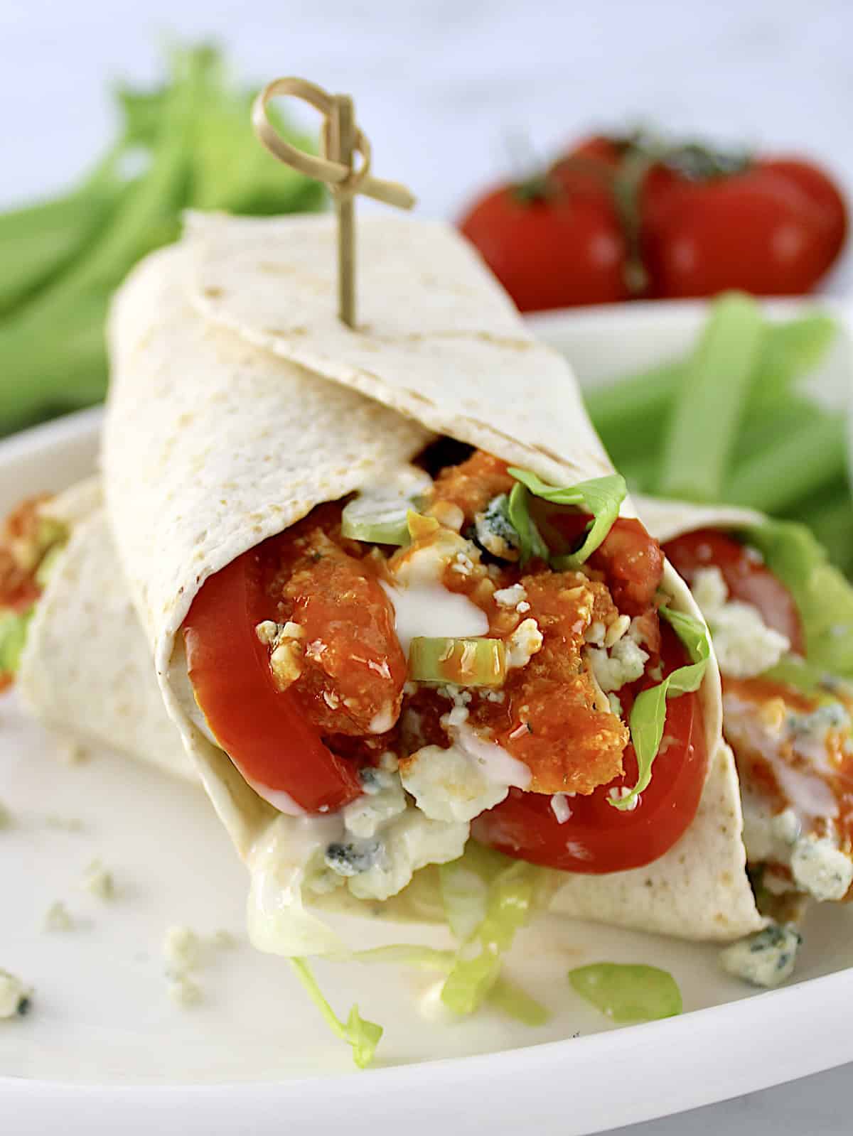 closeup of Buffalo Chicken Wrap on white plate with tomatoes and celery in back