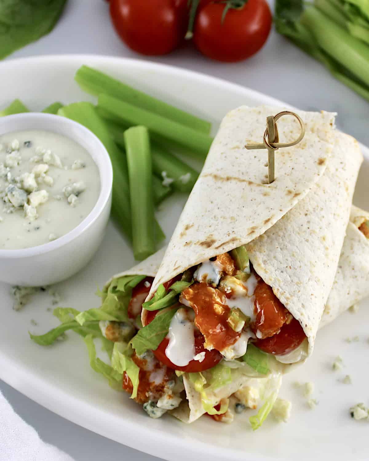 Buffalo Chicken Wrap cut in half on white plate with blue cheese and celery sticks on side