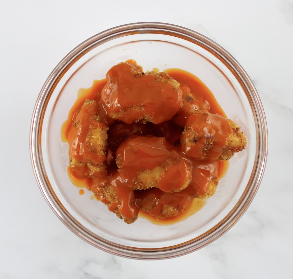 chicken nuggets in glass bowl with buffalo wing sauce drizzled on top