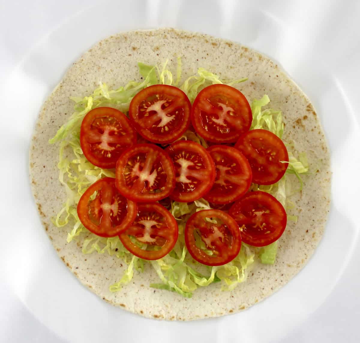 tortilla with shredded lettuce and slice tomatoes on top