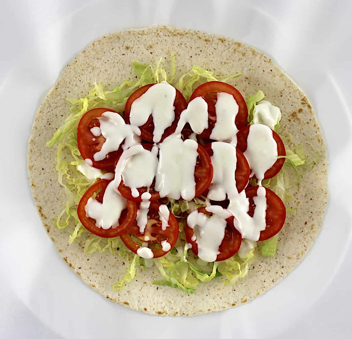 tortilla with shredded lettuce, blue cheese dressing and slice tomatoes on top