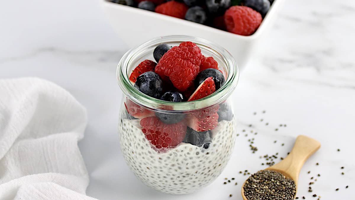 Chia Seed Pudding in glass open jar with fresh berries on top and in background