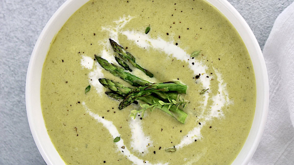 overhead view of Cream of Asparagus Soup with asparagus spears in center and swirl of cream around