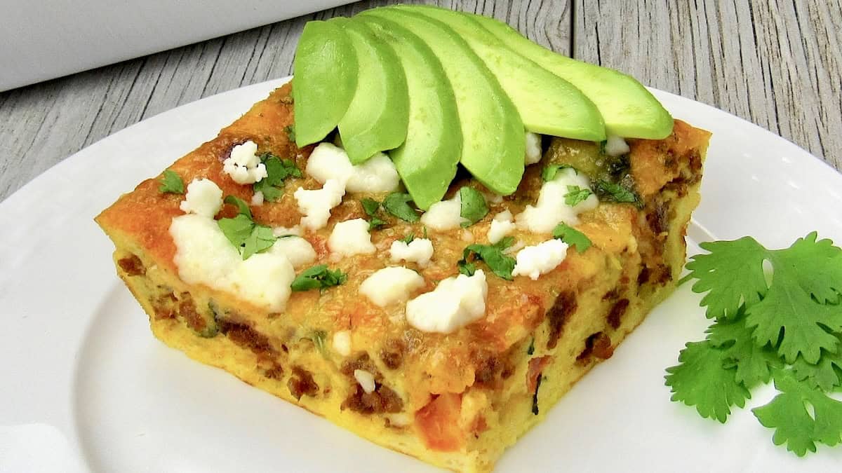 slice of Mexican Breakfast Casserole on white plate with sliced avocado on top