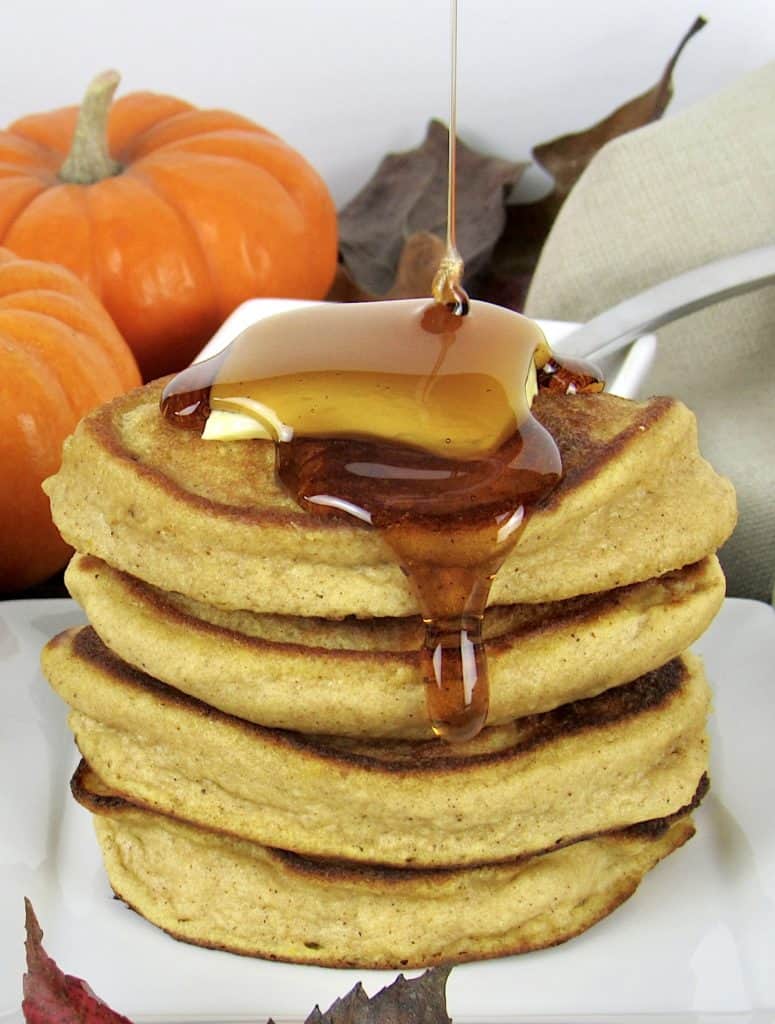 stack of Pumpkin Pancakes with pad of butter on top and maple syrup pouring over