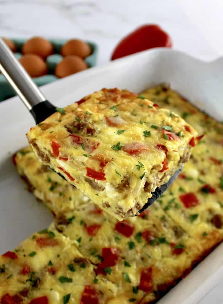 Sausage and Peppers Breakfast Casserole slice on spatula held up over casserole