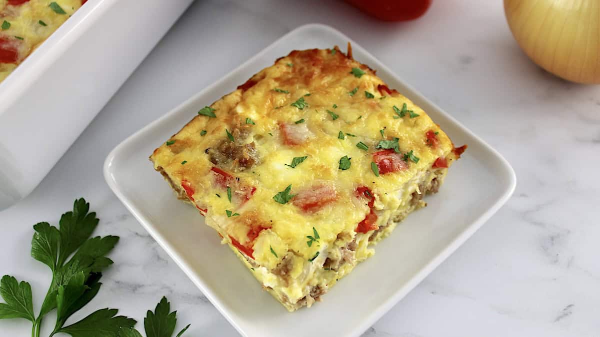 closeup of slice of Sausage and Peppers Breakfast Casserole on white square plate