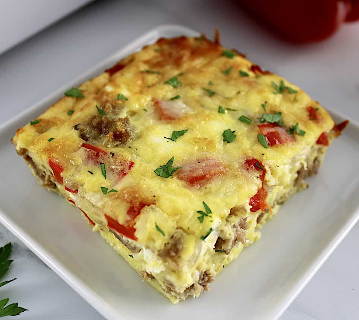 closeup of slice of Sausage and Peppers Breakfast Casserole on white square plate