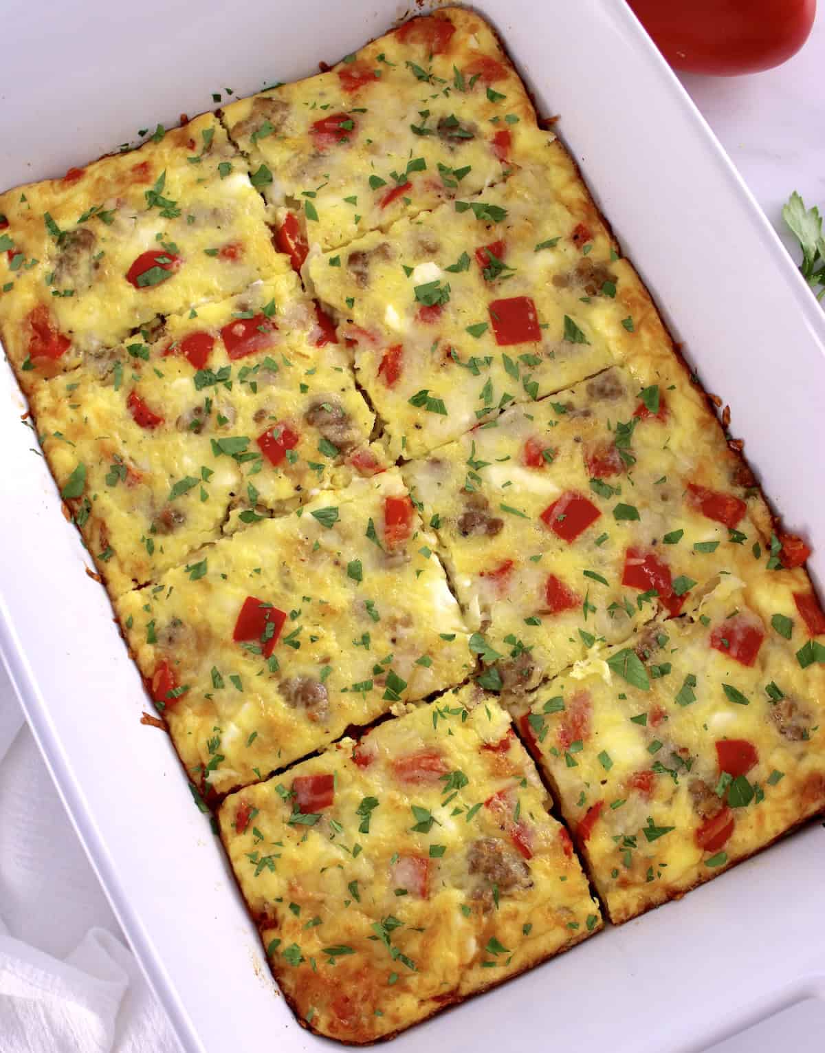 overhead view of Sausage and Peppers Breakfast Casserole cut into 8 slices in white baking dish