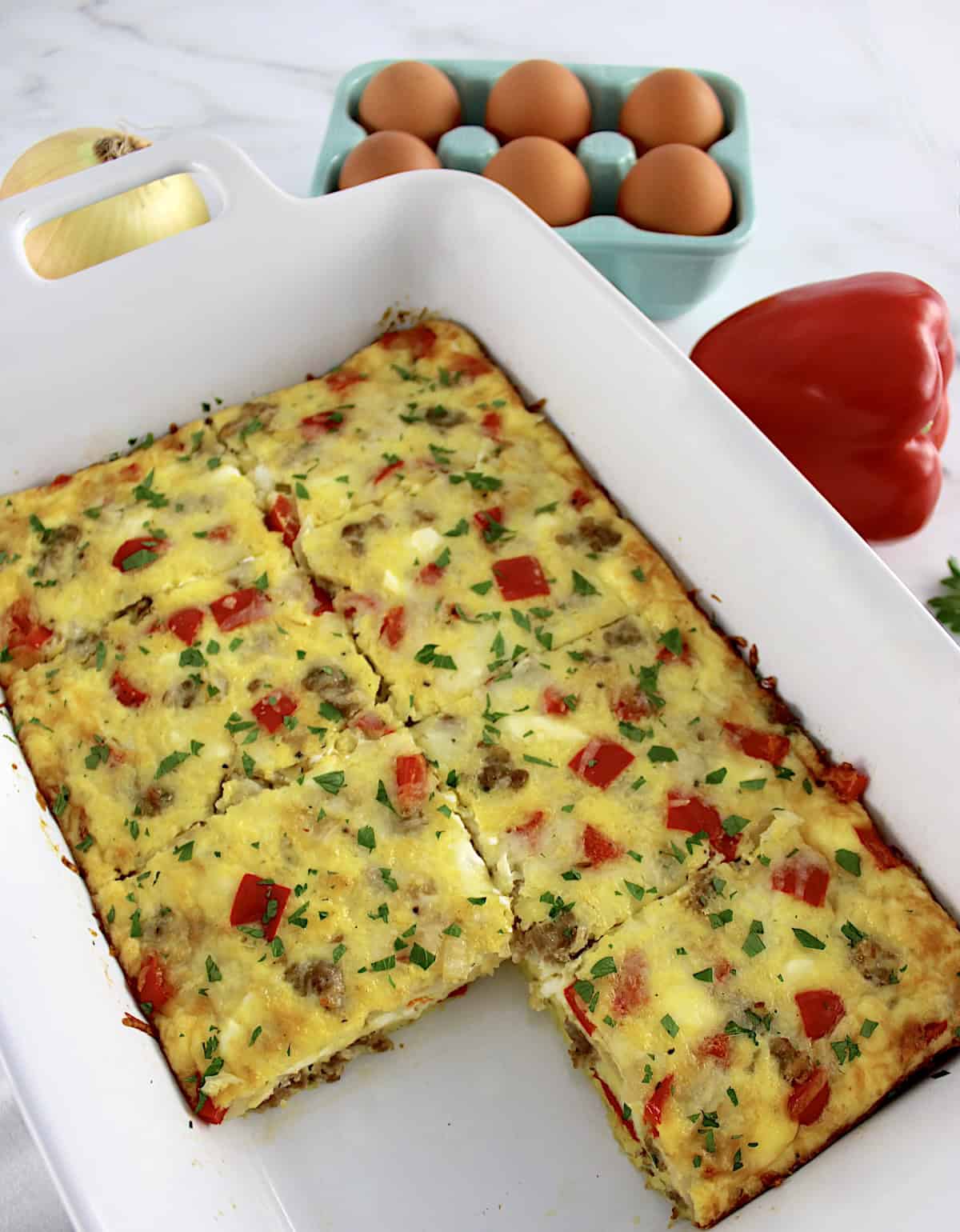 overhead view of Sausage and Peppers Breakfast Casserole in white casserole with slice missing