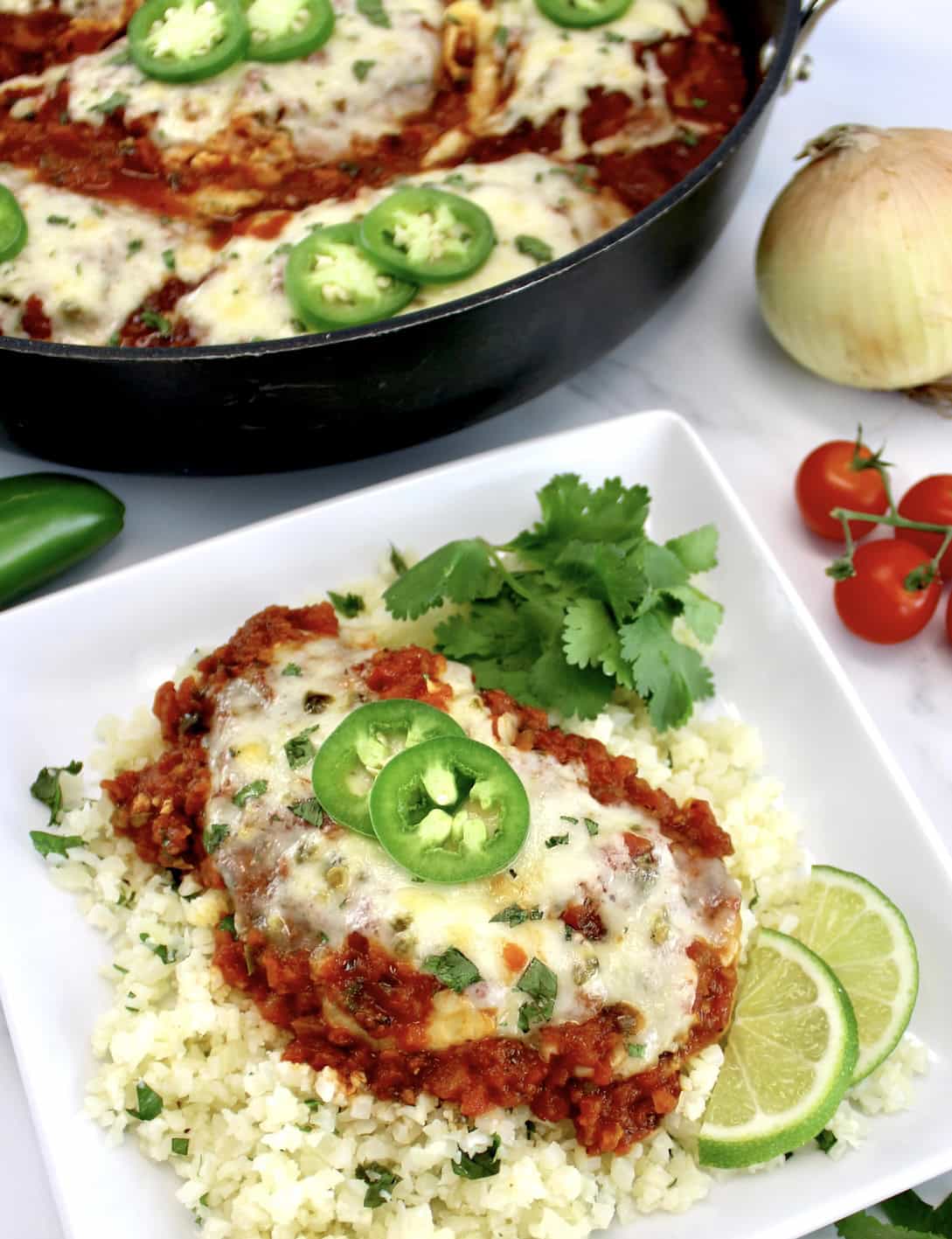 Skillet Salsa Chicken on white plate over lime cilantro cauliflower rice with skillet in back