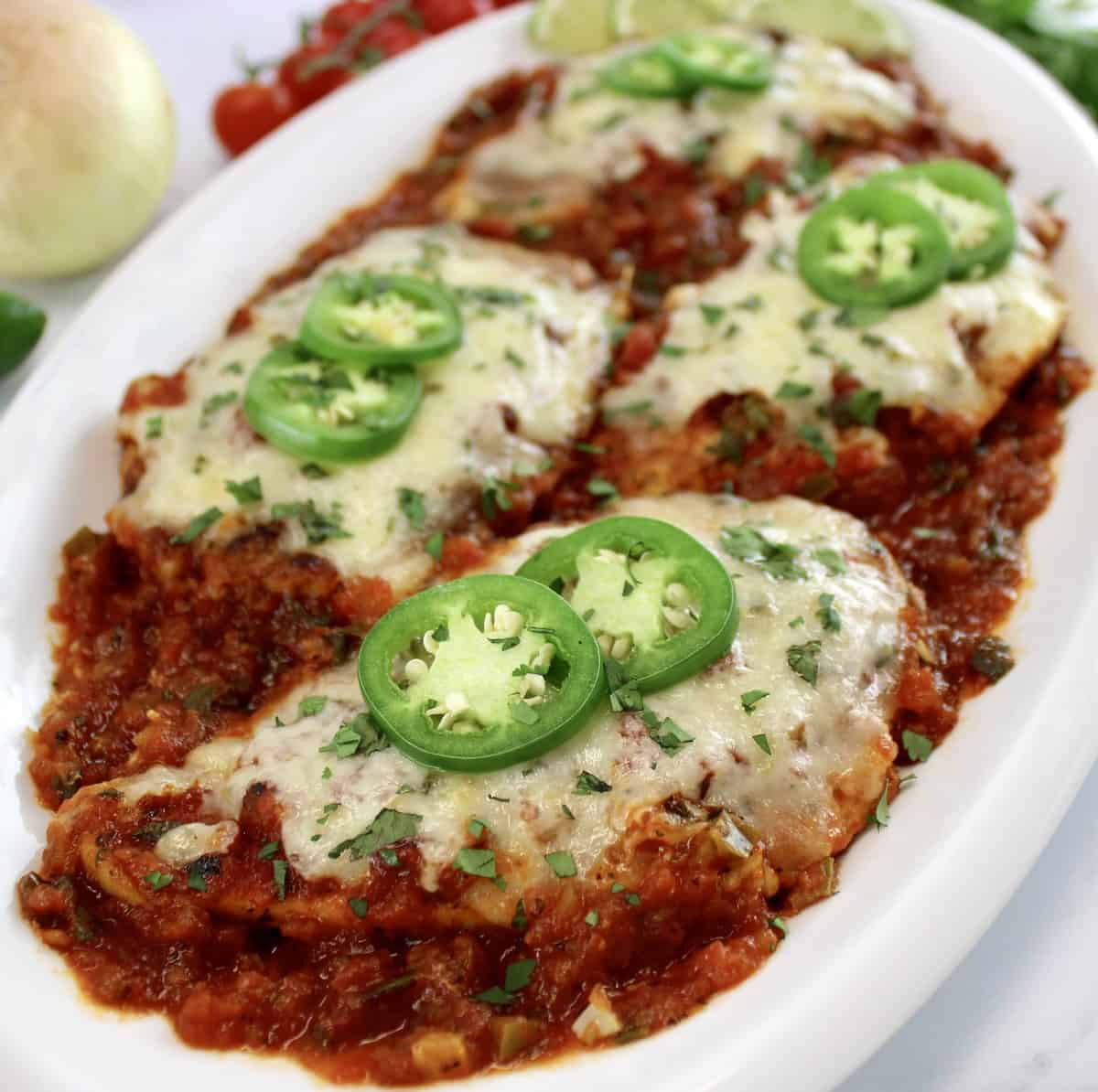 Skillet Salsa Chicken on white oval platter with 2 jalapeno slices on top of each