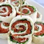 Smoked Salmon Pinwheels stacked up on white plate with one in front