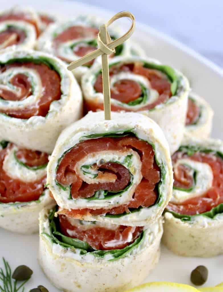 Smoked Salmon Pinwheels stacked up on white plate with one in front