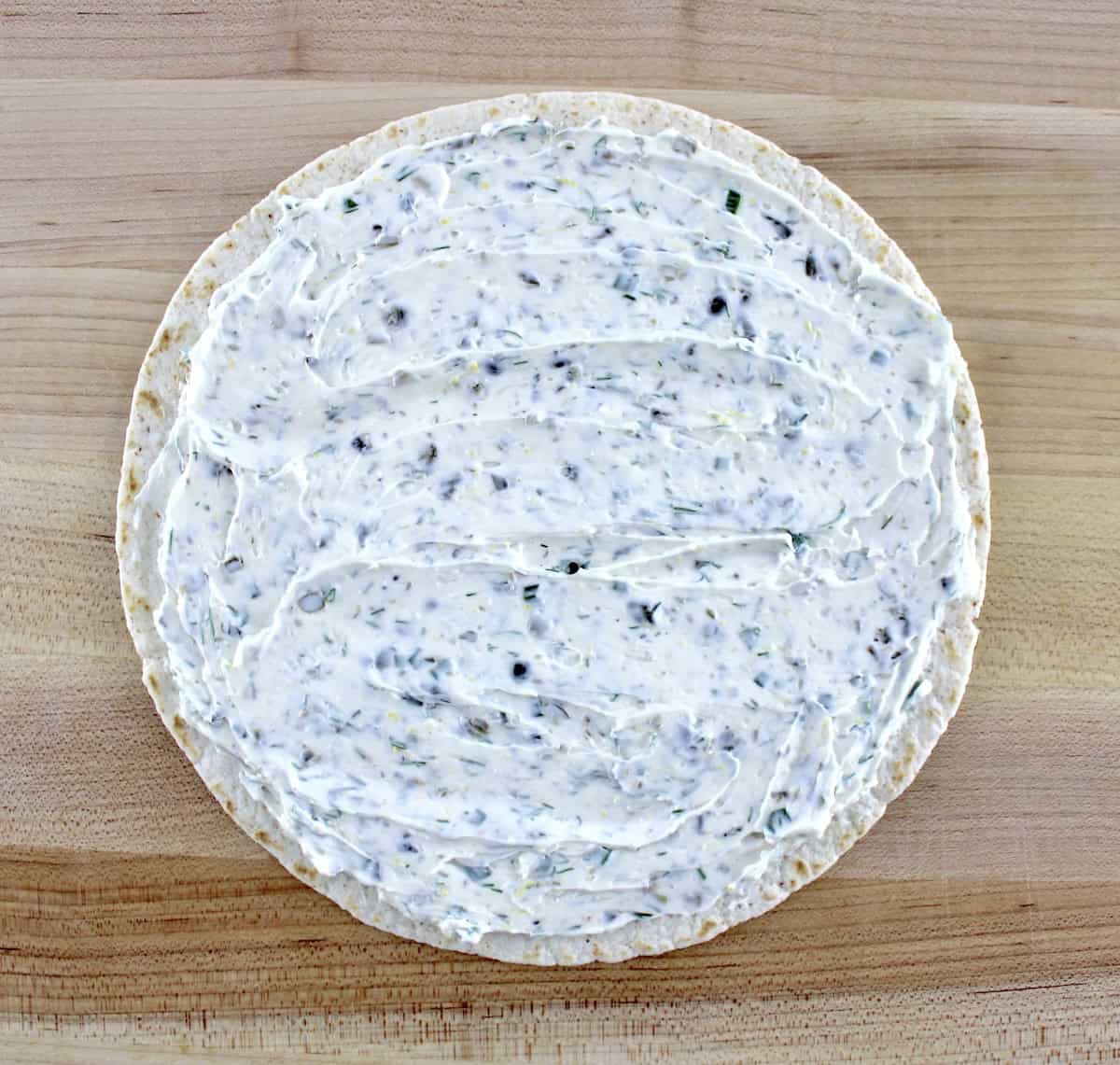 tortilla on cutting board with cream cheese spread on top