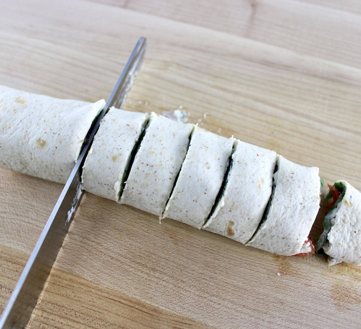 Smoked Salmon Pinwheels being sliced with bread knife on cutting board