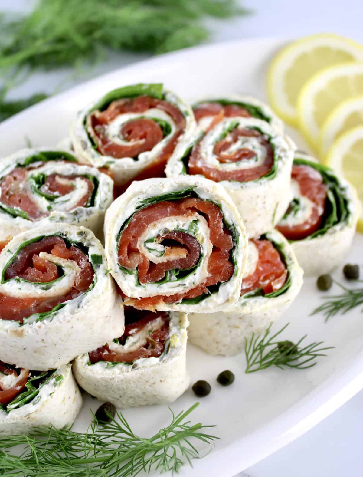 Smoked Salmon Pinwheels stacked up on white plate with one in front upright