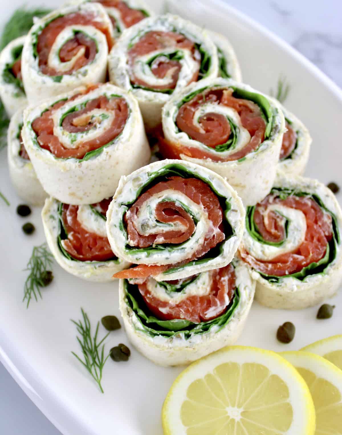 Smoked Salmon Pinwheels stacked up on white plate with one in front upright