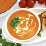 Tomato Bisque in white bowl with grilled cheese, tomatoes and skillet on side