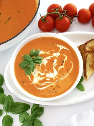 Tomato Bisque in white bowl with grilled cheese, tomatoes and skillet on side