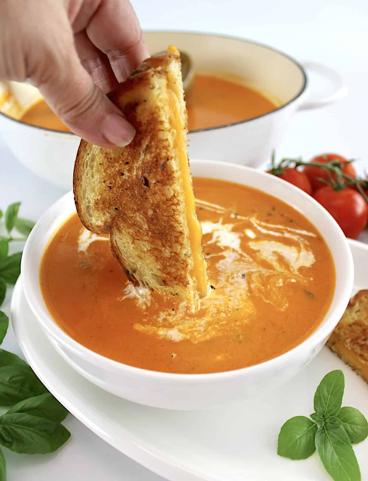 half grilled cheese being dipped into Tomato Bisque in white bowl