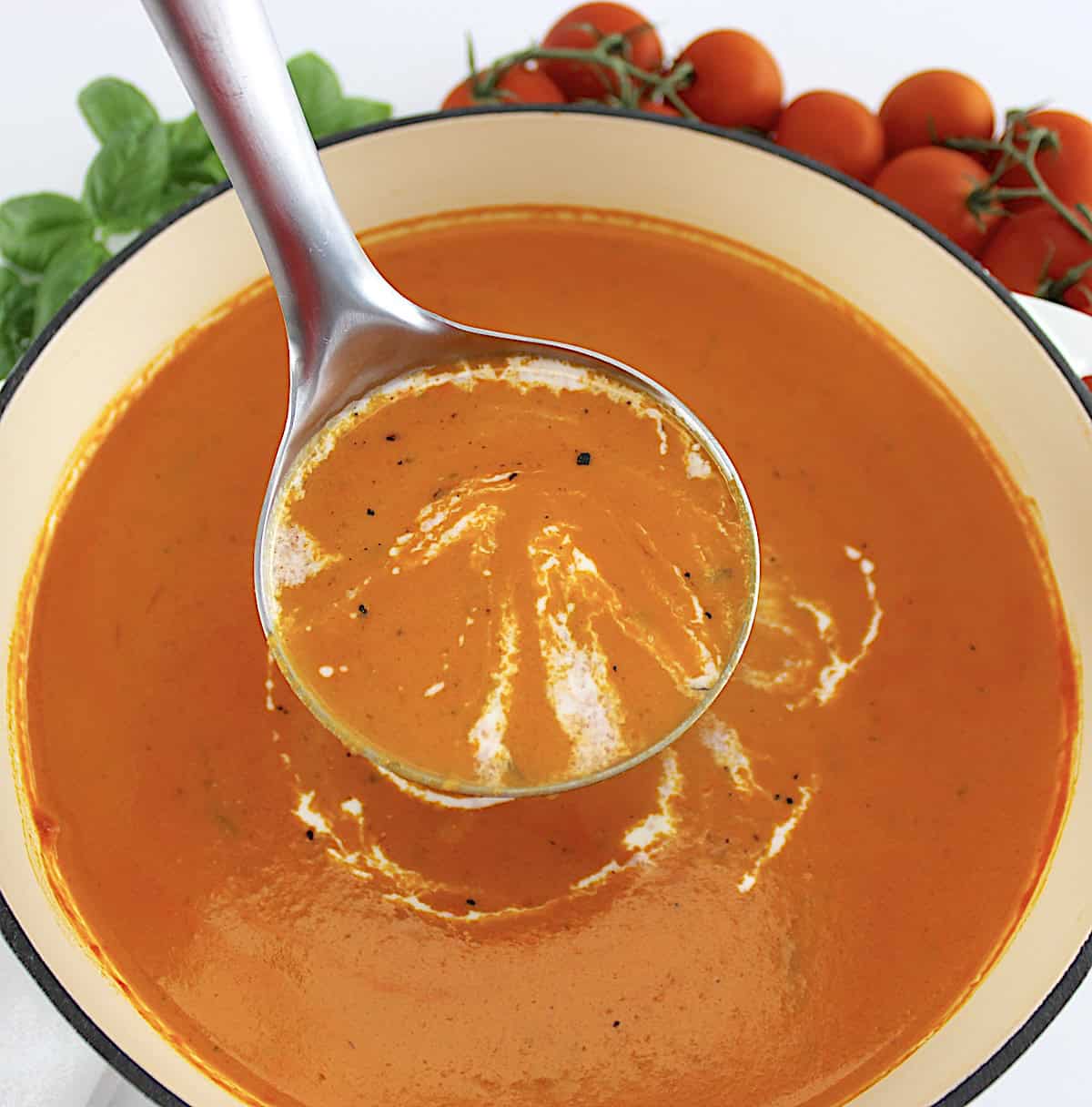 Tomato Bisque with heavy cream drizzle in pot with silver ladle