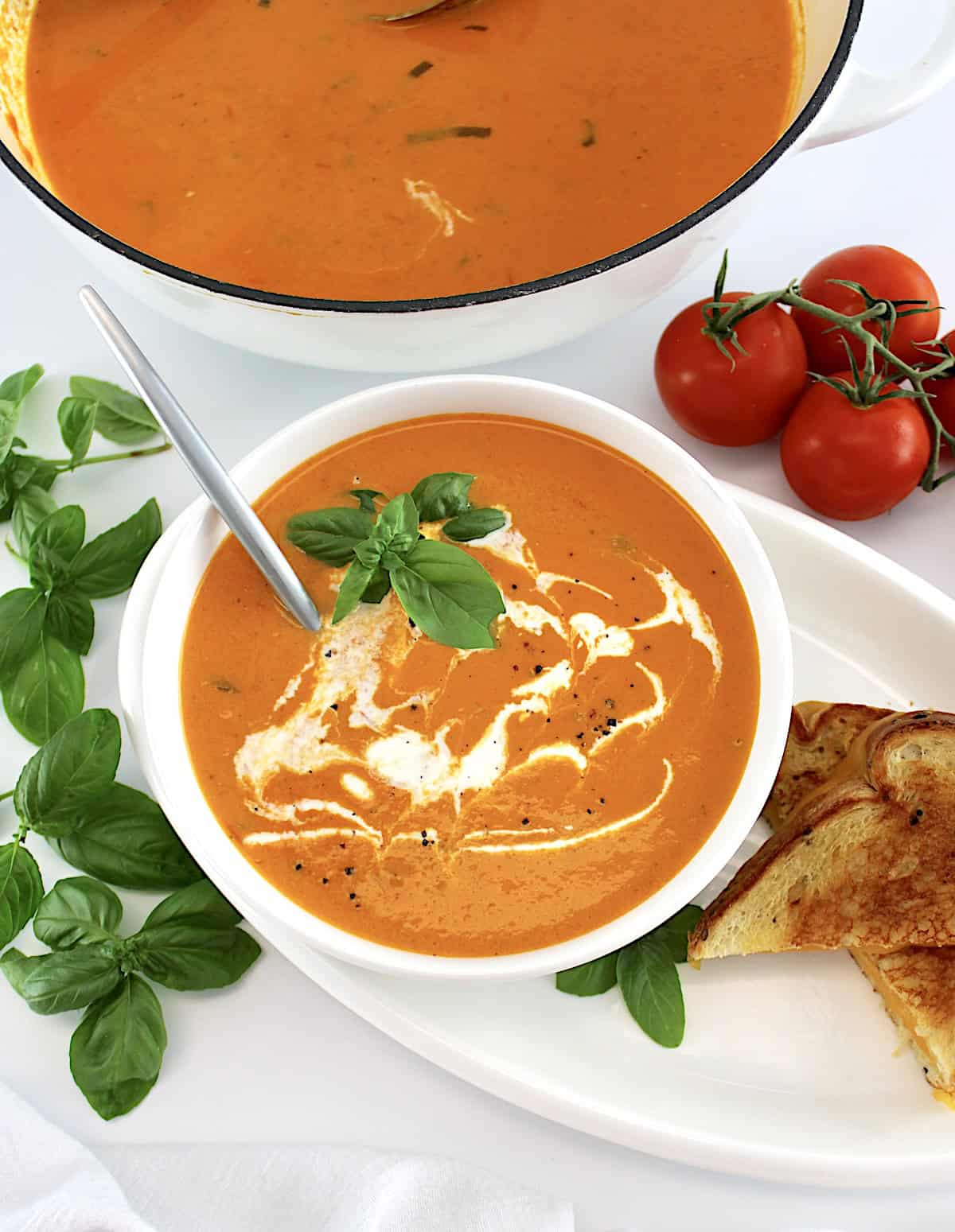 Tomato Bisque in white bowl with spoon and pot in back