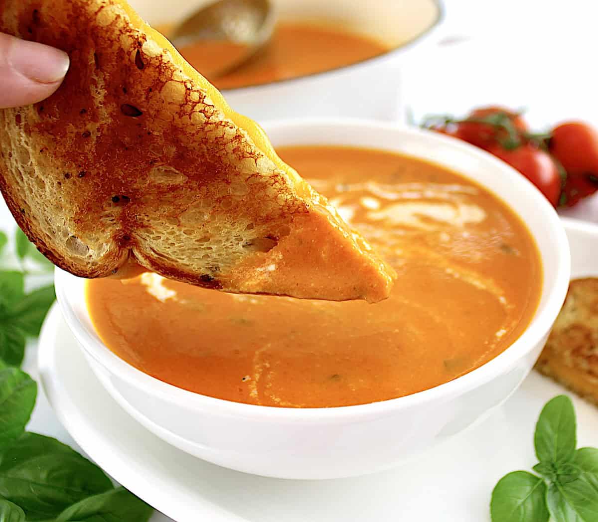 grilled cheese being dipped into Tomato Bisque in white bowl