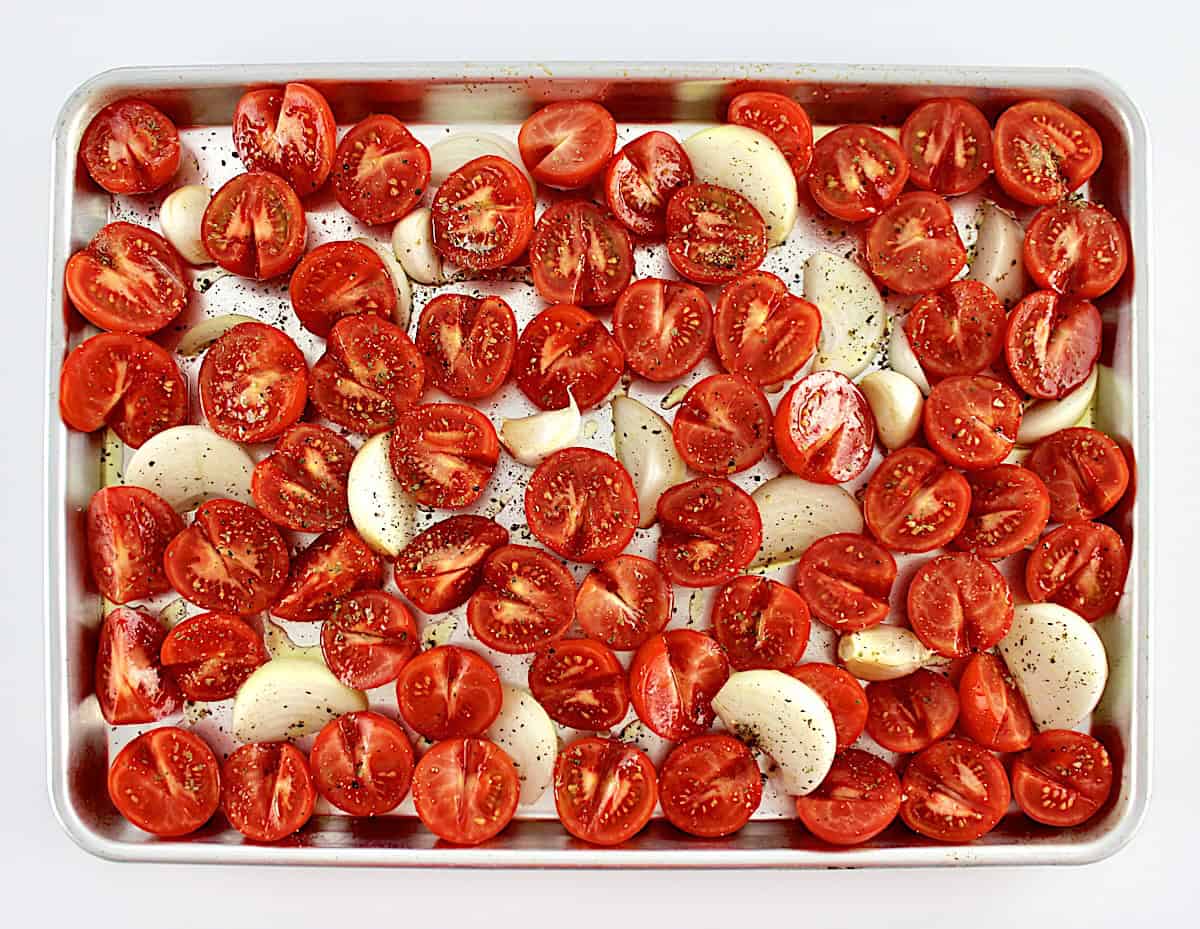 halved tomatoes, sliced onions and garlic cloves on baking sheet with olive oil and dried oregano