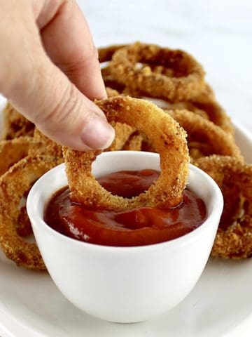 Air Fryer Onion Ring being dipped into ketchup in white cup