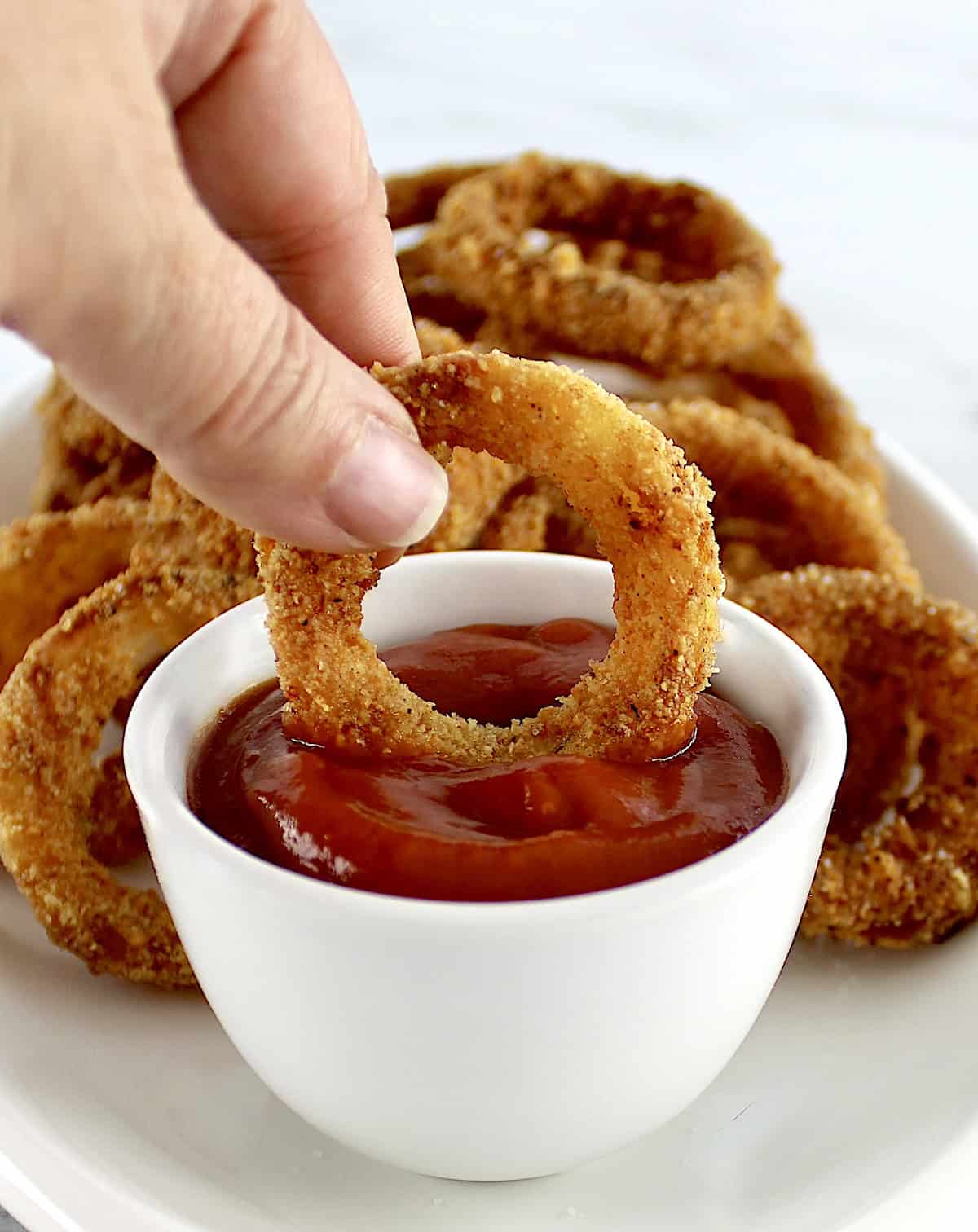 Air Fryer Onion Ring being dipped into ketchup in white cup