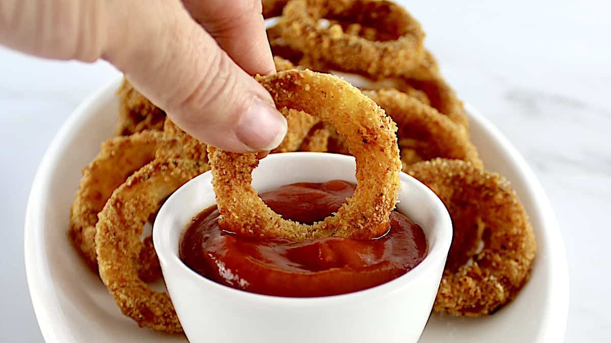 Air Fryer Onion Ring being dipped into ketchup in white cup