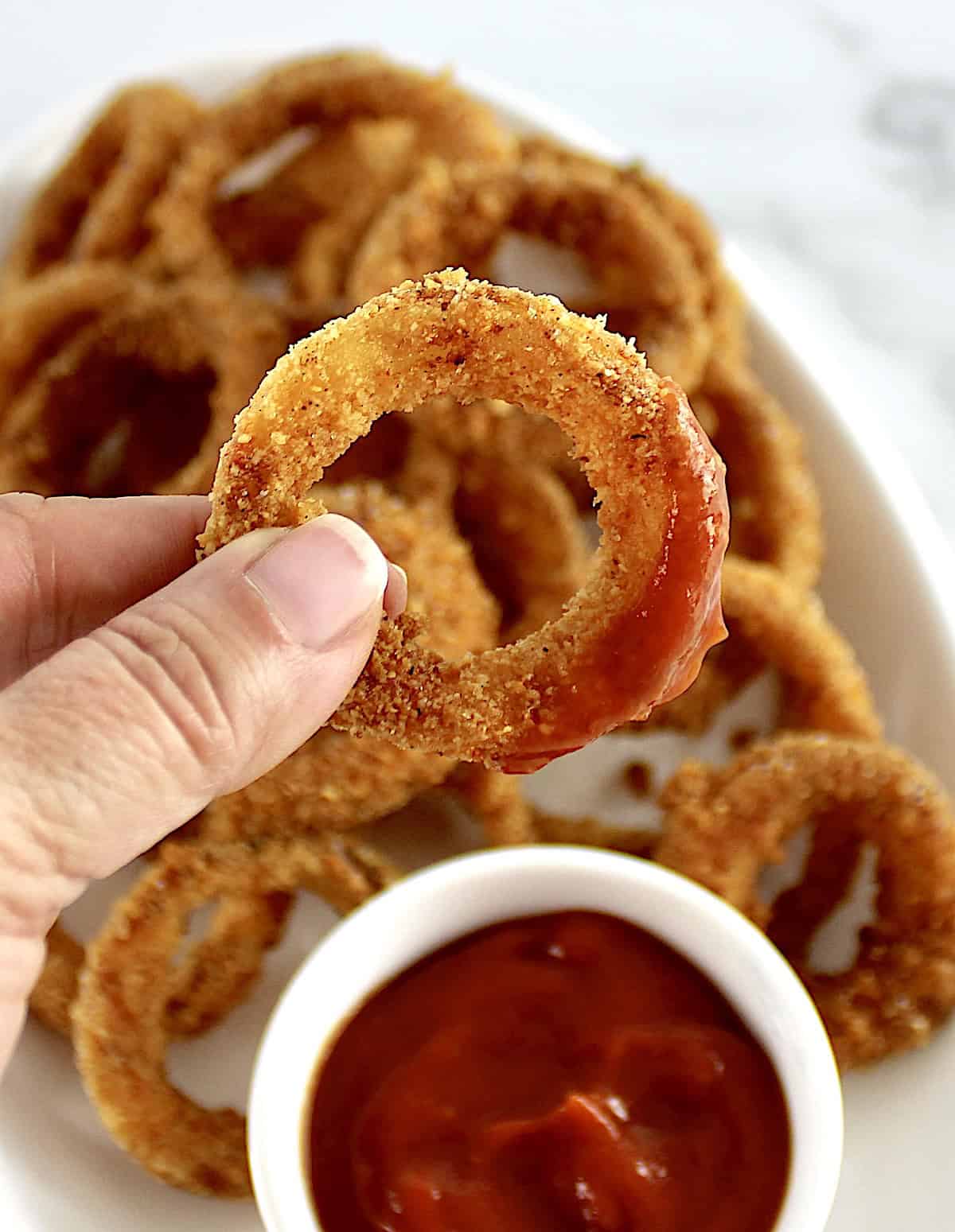 Air Fryer Onion Ring being held up with ketchup on the end